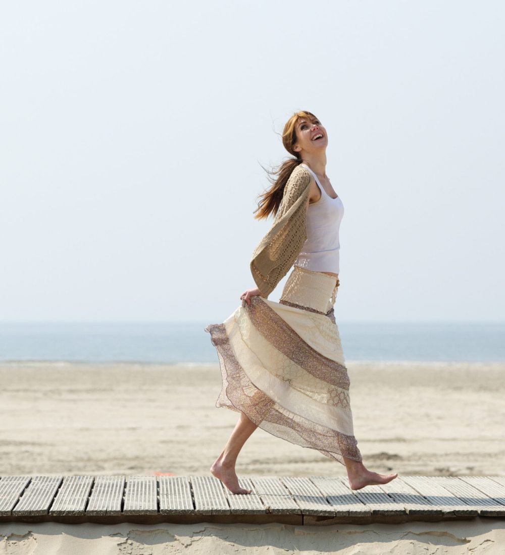 Full length portrait of a carefree middle aged woman walking barefoot at the beach